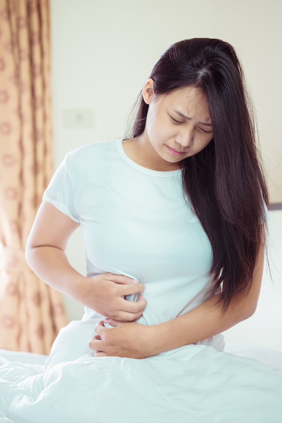 Asian Young Woman Suffering from Abdominal Pain While Sitting on